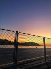 Sunset Behind Chain-Link Fence and Distant Coastline