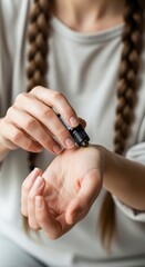 Obraz premium A person with braided hair applies essential oil from a small dropper bottle onto their wrist.