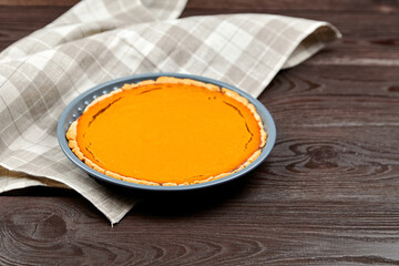 Freshly baked pumpkin pie on a blue plate rests on a rustic wooden table, surrounded by a checkered...