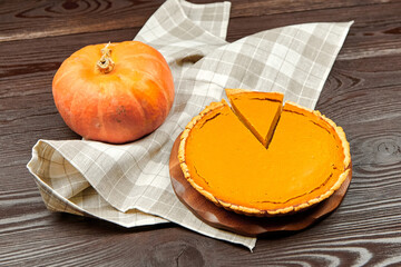Freshly baked pumpkin pie on a wooden table, accompanied by a whole pumpkin and a checkered cloth, showcasing autumn flavors and seasonal ingredients for festive occasions