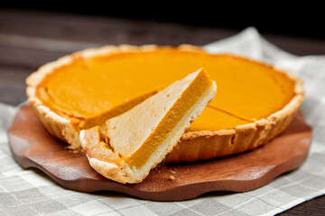 Delicious pumpkin pie on a wooden serving board, with a slice removed, showcasing the creamy...