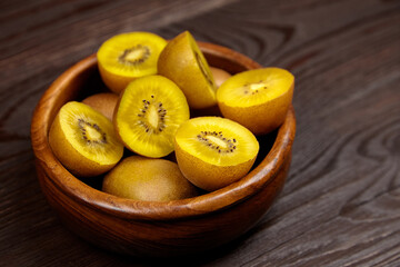 Yellow gold kiwi fruit halves and whole fruits arranged in a wooden bowl on a rustic wooden table,...