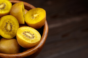Yellow gold kiwi fruit halves and whole fruits arranged in a wooden bowl, showcasing vibrant colors...