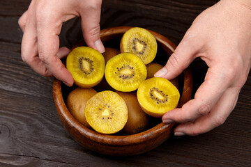 Yellow gold kiwi fruit displayed in a wooden bowl, hands gently arranging the sliced pieces,...