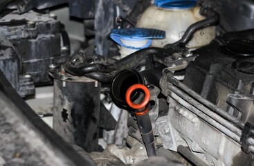 Auto engine bay close-up: open oil filler neck, orange dipstick loop, tangled hoses, blue capped coolant tank, dusty aluminum block, grime hinting at overdue maintenance risks
