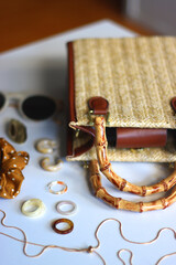 Wicker purse, sunglasses, scrunchie, lipstick and various gold and neutral jewelry on white background. Selective focus.