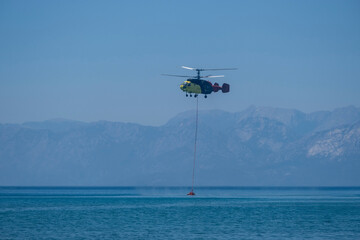 Firefighting helicopter drawing water from the sea to extinguish the forest fire