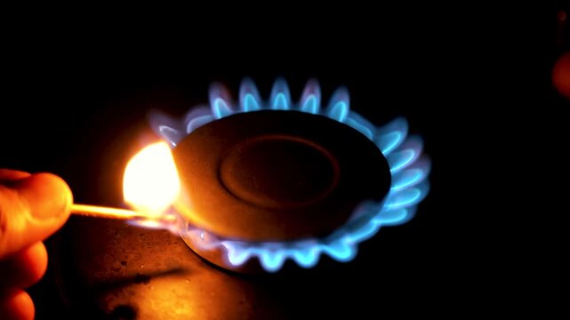A hand lighting a gas stove burner with a match