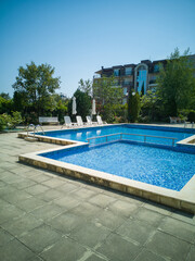 Clean outdoor pool with clear blue water, sun loungers, and umbrellas near modern apartment building. Peaceful summer vibe and relaxation area.