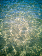 Transparent turquoise sea water with sunlight patterns on sandy bottom. Soft wave ripples and...