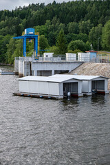 Three metal boat garages floating on a lake near a hydroelectric facility with concrete dam, blue...