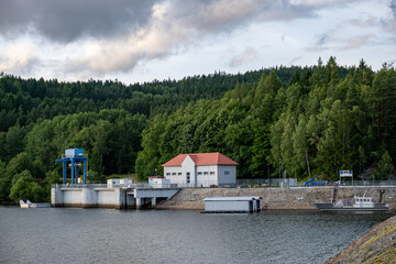 Hydropower dam with a small white building and red roof, located by the forest. Blue crane...