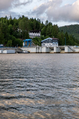 Vertical shot of a hydroelectric dam with technical structures and houses in a forested hillside,...