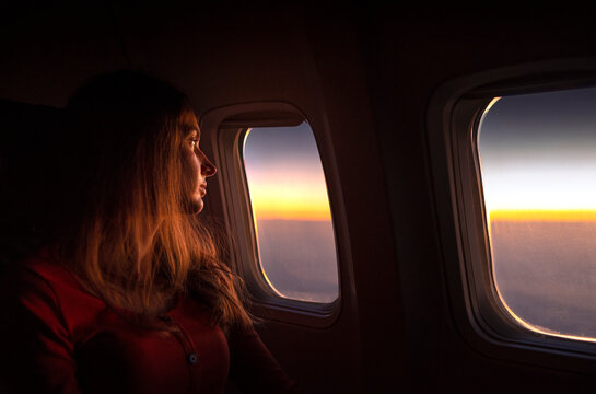 Young woman gazing out airplane window at sunrise during flight. Peaceful travel moment, early morning sky