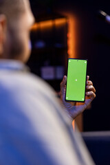 Black remote worker looking at green screen on his device at home, relaxing in the living room and solving his freelancing tasks. Young adult being casual in his trendy apartment, teleworking.