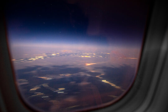 Blurred night aerial cityscape view through airplane window at twilight. Motion blur and glowing lights create dreamy atmosphere of air travel
