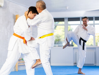 Elderly man and young guy sparring during karate classes in the gym under the guidance of a coach