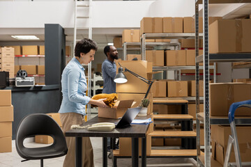 Young woman at her desk reviewing shipment data for delivery services, verifying taped boxes in a...