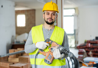 Confident man construction worker standing with pneumatic hammer drill on indoor building...