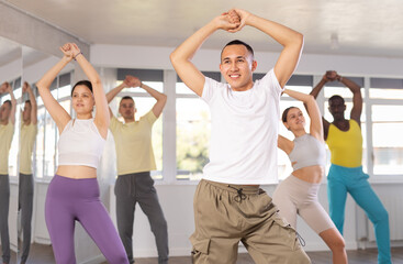 Expressive young Asian male instructor in white t-shirt and cargo pants leading modern dance...