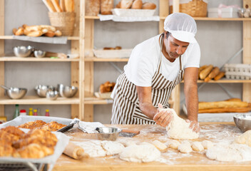 Caucasian guy works in bakery as baker, kneads dough, works with flour. Working moment, process of creating croissants in bakery