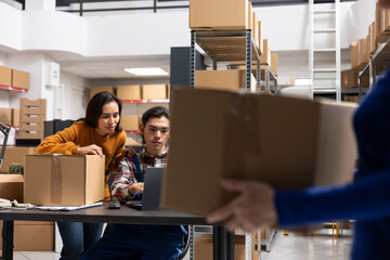 Workers team processing orders and retail shipments in small storehouse with taped boxes and...