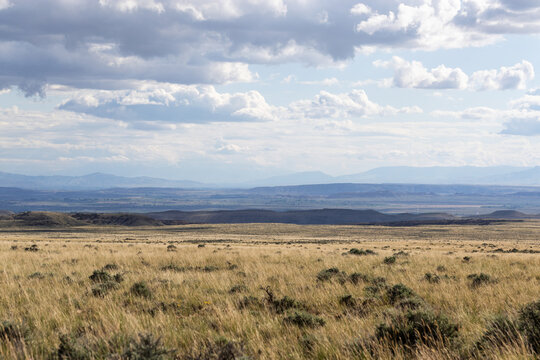 Scenic vista showing grassy prairie with layers of mountains and hills in the distance under a stormy sky with dark  nimbostratus nimbus rain clouds creating haze far away