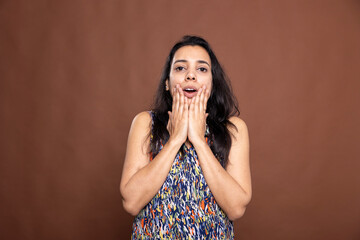 Stunned Indian woman with hands on cheeks and eyes wide open, expressing dramatic disbelief....