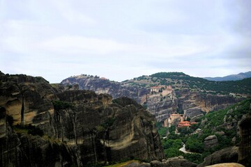 Obraz premium Panoramic view of the Meteora monasteries built on dramatic sandstone rock formations in Greece. Historic Orthodox architecture, green forested valleys and rugged cliffs create an iconic travel landsc
