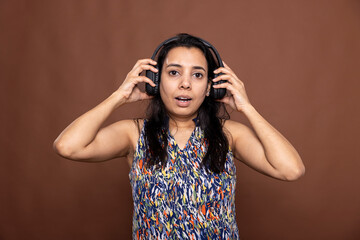 Portrait of female model wearing headphones, reacting to surprising audio content with an...