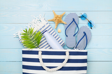 Blue beach bag with summer accessories on wooden background, top view