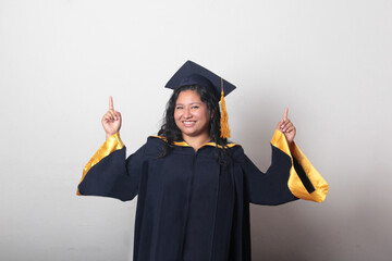 Young brunette Latina woman wearing a cap and gown celebrates her graduation and the completion of...