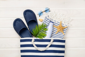 Blue beach bag with summer accessories on wooden background, top view
