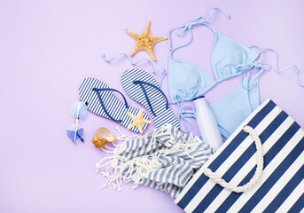 Blue bikini with beach accessories on color background, top view