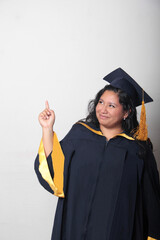 Young brunette Latina woman wearing a cap and gown celebrates her graduation and the completion of...