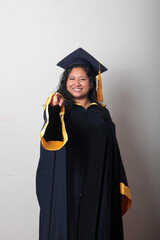 Young brunette Latina woman wearing a cap and gown celebrates her graduation and the completion of...