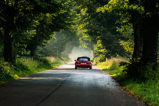 Braniewo, Poland - August 16, 2021. Red convertible Mazda MX5 going on the tar road through parkway in sunset