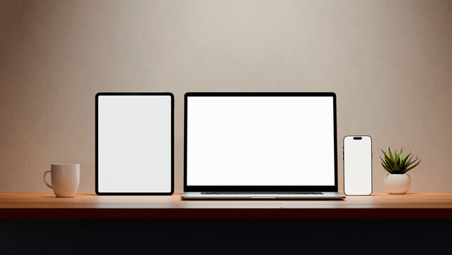 Laptop, mobile phone and tablet with blank screen for responsive Web Design and website Mockup. Digital devices over an office wooden desk.