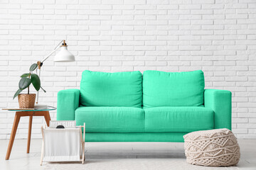 Interior of living room with green sofa near white brick wall