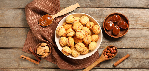 Bowl with tasty walnut shaped cookies, boiled condensed milk, hazelnuts and almonds on wooden table