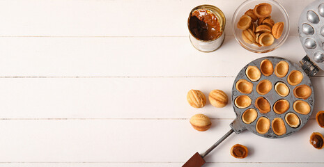 Baking form with tasty walnut shaped cookies and tin can of boiled condensed milk on white wooden...