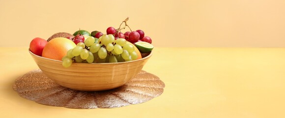 Bowl full of different fresh fruits on color background with space for text