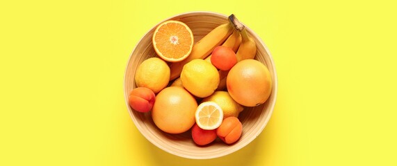 Bowl full of different fresh fruits on yellow background, top view