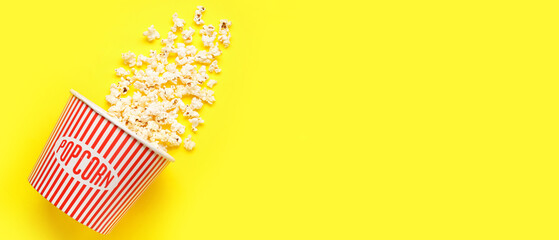 Bucket with tasty popcorn on yellow background