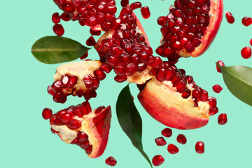 Flying fresh pomegranates with seeds and leaves on turquoise background