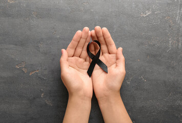 Woman holding black funeral ribbon on grey background