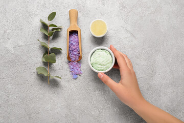 Female hand with body scrubs, sea salt and eucalyptus branch on grunge background