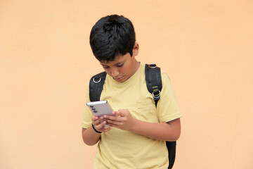 A 10-year-old Latino boy uses his cell phone to play video games, make video calls, send messages,...