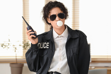 African-American police officer with radio transmitter blowing bubble gum in office