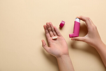 Child's hands with asthma inhaler and pill on beige background